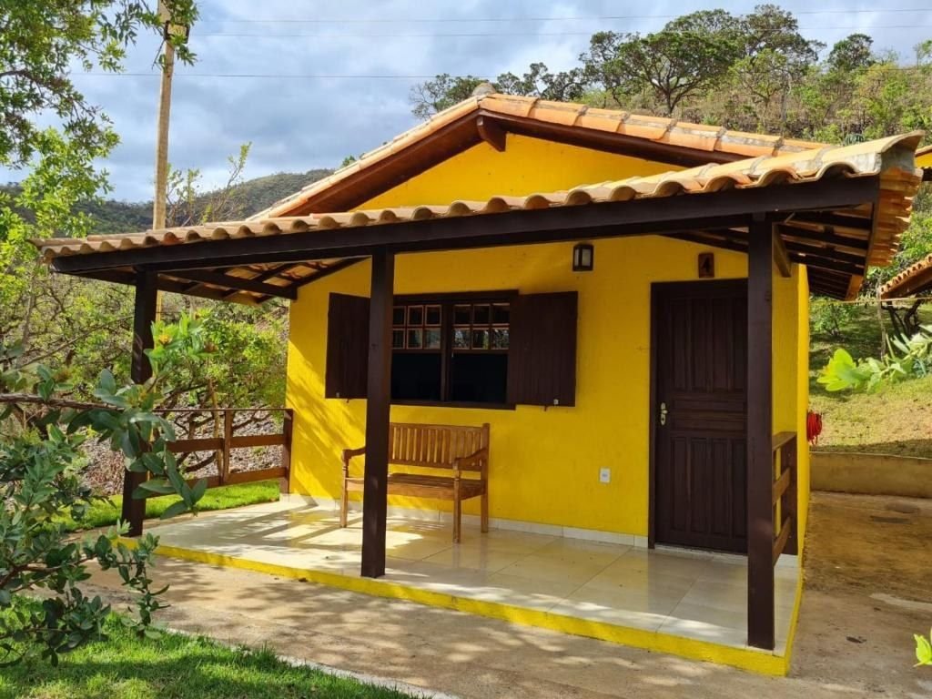 Fachada amarela do chalé com varanda, banco e portas de madeira